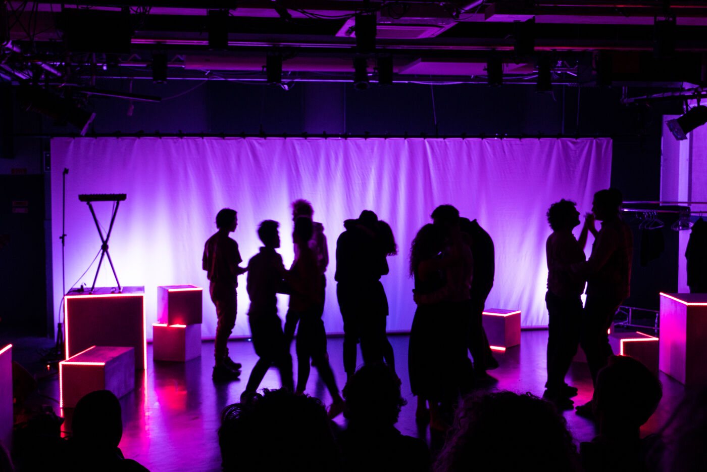 Wide shot of the stage in purple light, the full company on stage among the cubes